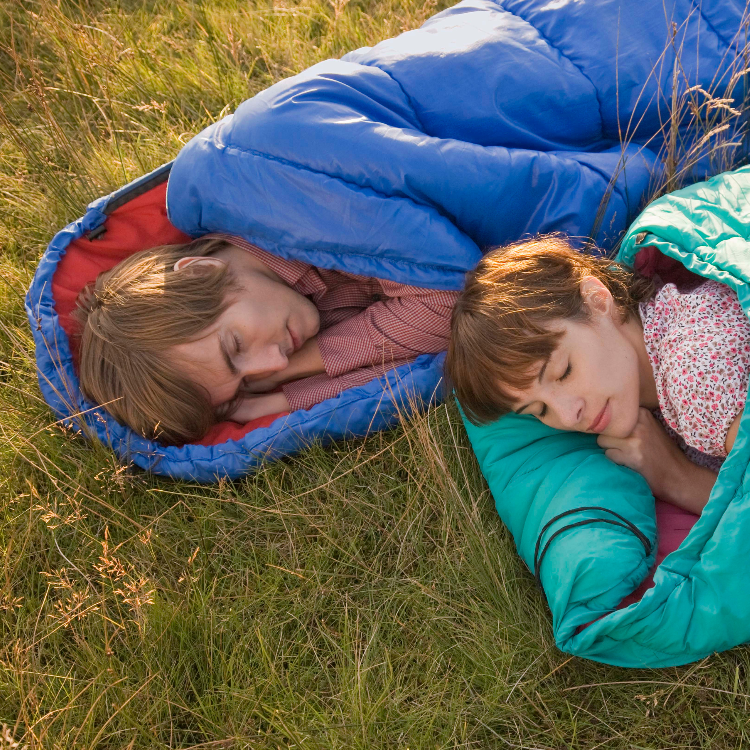 mage of a camping scene with a person sleeping on an air bed and another person sleeping in a sleeping bag on the ground.